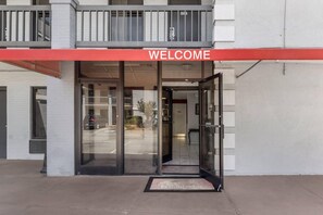 A building entrance with a 'WELCOME' sign, glass doors, and a small outdoor area with a mat. - Econo Lodge Research Triangle Park (Durham)