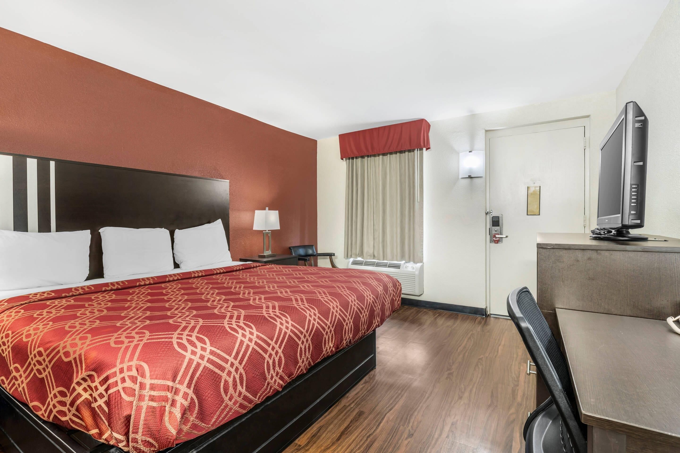 Habitación de hotel con cama, escritorio, silla, televisión y ventana con cortinas.