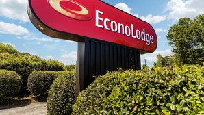 Un letrero grande y rojo con el texto 'EconoLodge', sobre un fondo de vegetación exuberante y un cielo azul despejado.