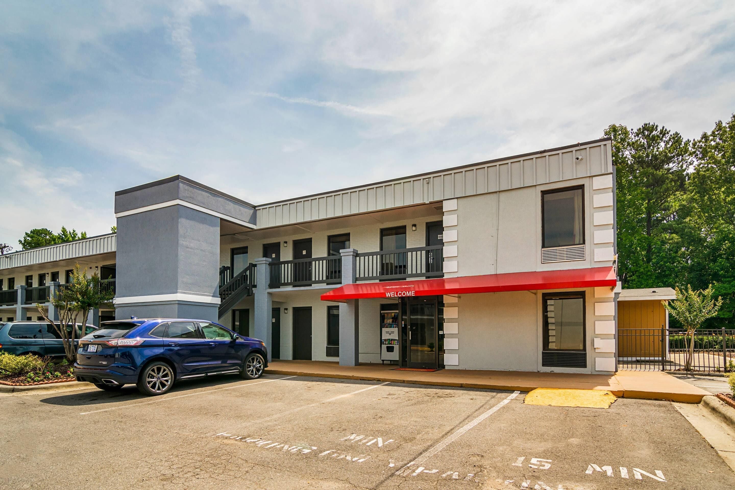 A modern building with a red awning, a parking lot, and a blue car parked in front.