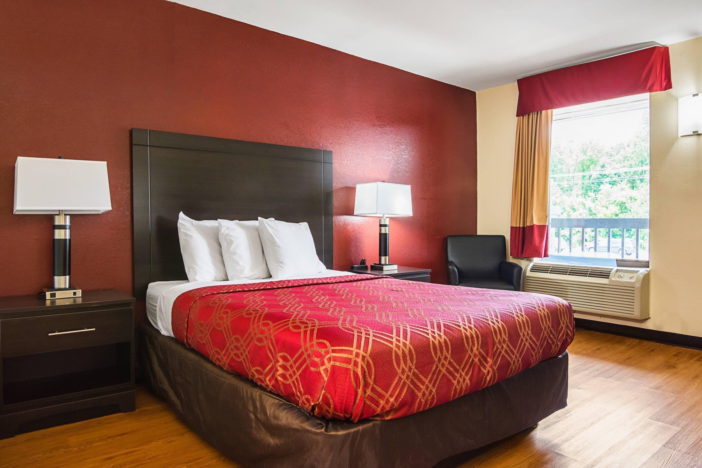 Une chambre d’hôtel avec un grand lit, deux tables de chevet, une chaise, une fenêtre avec des rideaux et un appareil de climatisation.