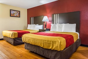 Quarto de hotel com duas camas, uma parede vermelha, piso de madeira e um quadro na parede.