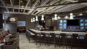 Zona de bar moderna con una barra alargada, varios taburetes y una pantalla de televisión sobre la barra.