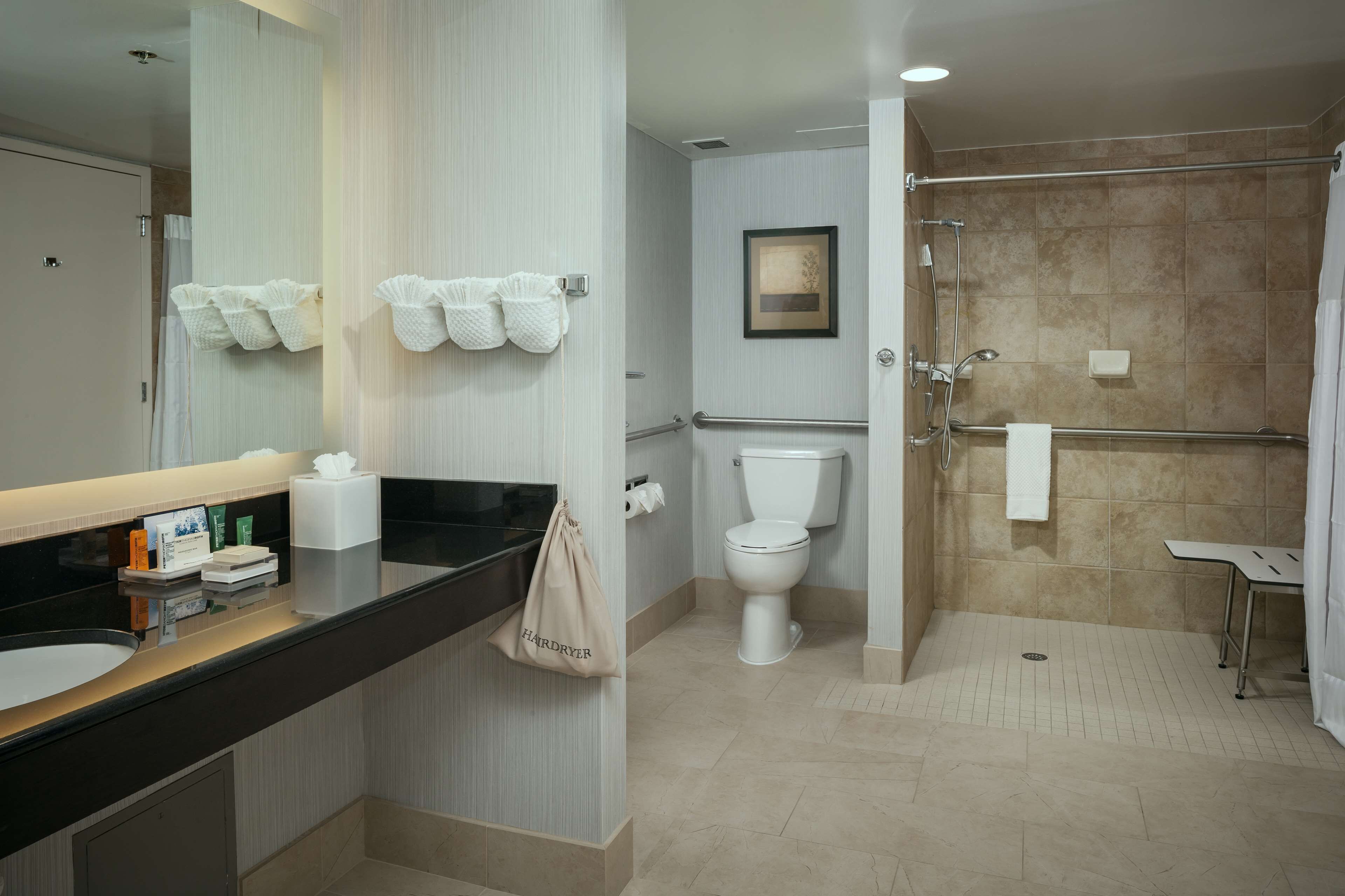Une salle de bain moderne avec un plan de toilette noir, des serviettes blanches, des toilettes et un espace douche.