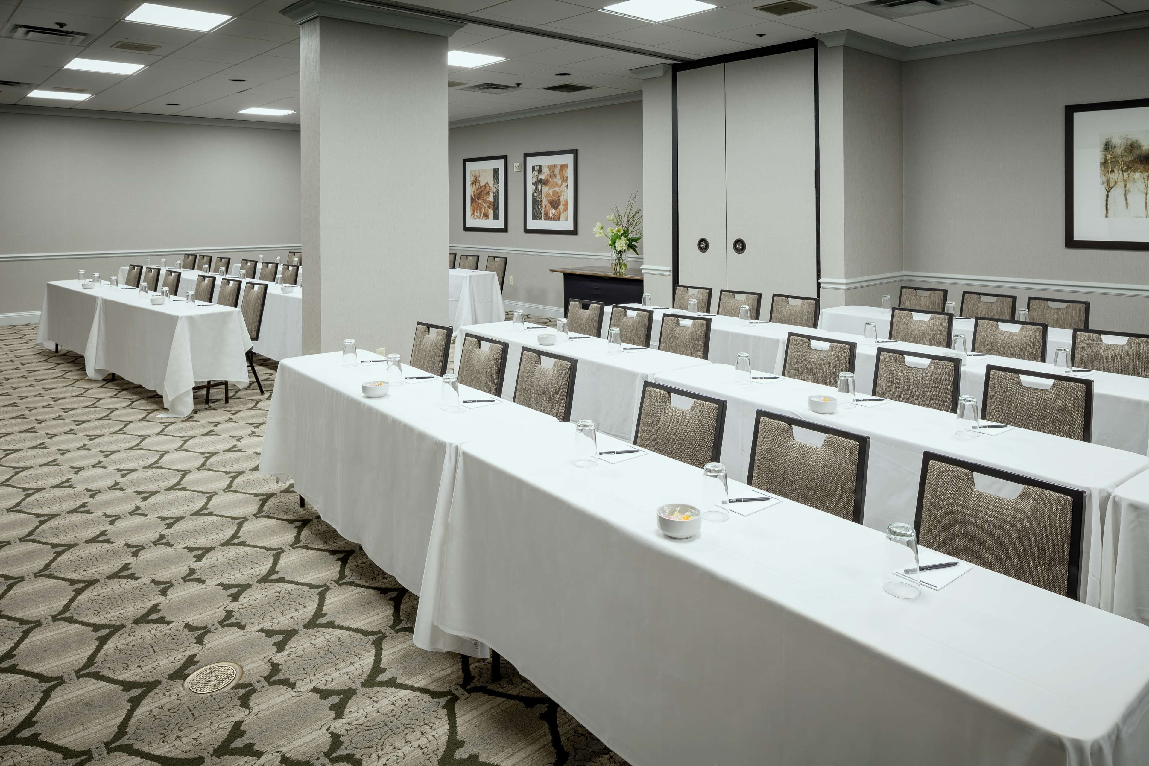 A conference room with long tables, chairs, and a patterned carpet.