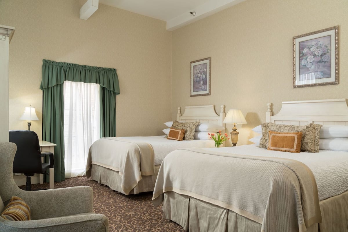 A hotel room with two beds, a desk, a chair, and two lamps.