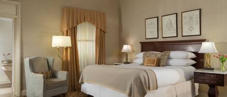 A hotel room with a large bed, two bedside lamps, a chair, a nightstand, and framed pictures on the wall.