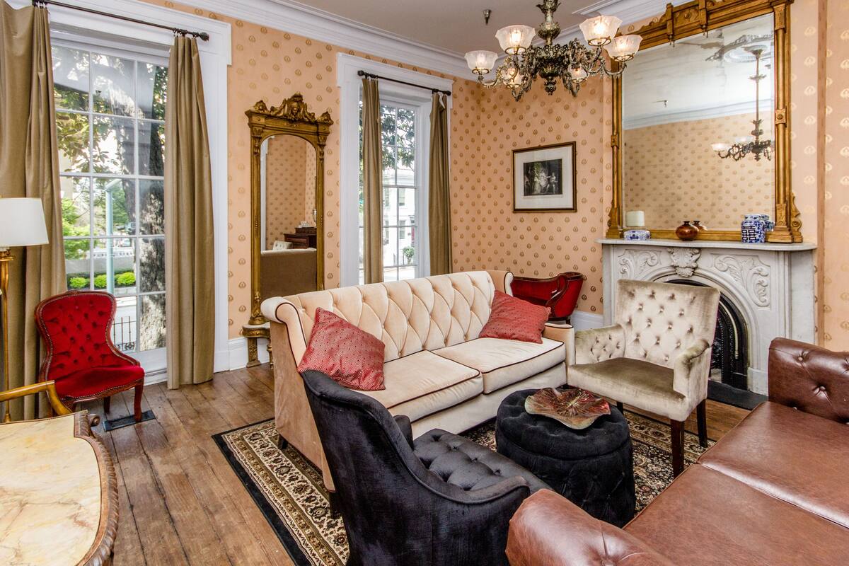 A room with a beige sofa, a red chair, a black ottoman, a wooden table, and a fireplace.