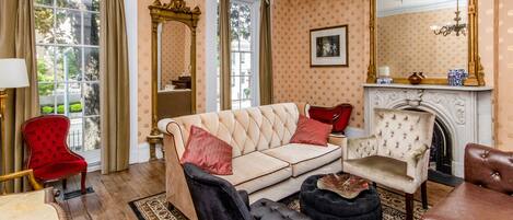 A room with a beige sofa, a red chair, a black ottoman, a wooden table, and a fireplace.