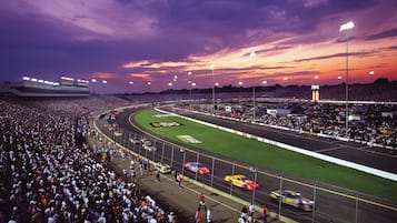Um estádio grande cheio de espectadores, uma pista de corrida e vários carros de corrida.