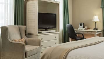 A hotel room with a bed, a TV, a desk with a lamp, a chair, and a coffee maker.