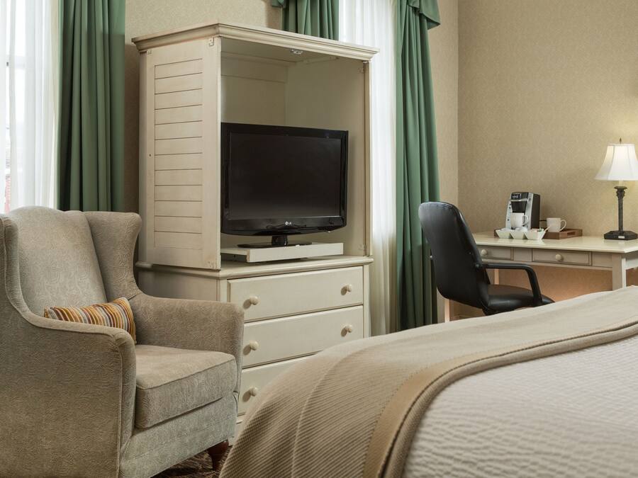 Habitació d'hotel amb un llit, una televisió, escriptori amb una làmpada, una cadira i una cafetera.