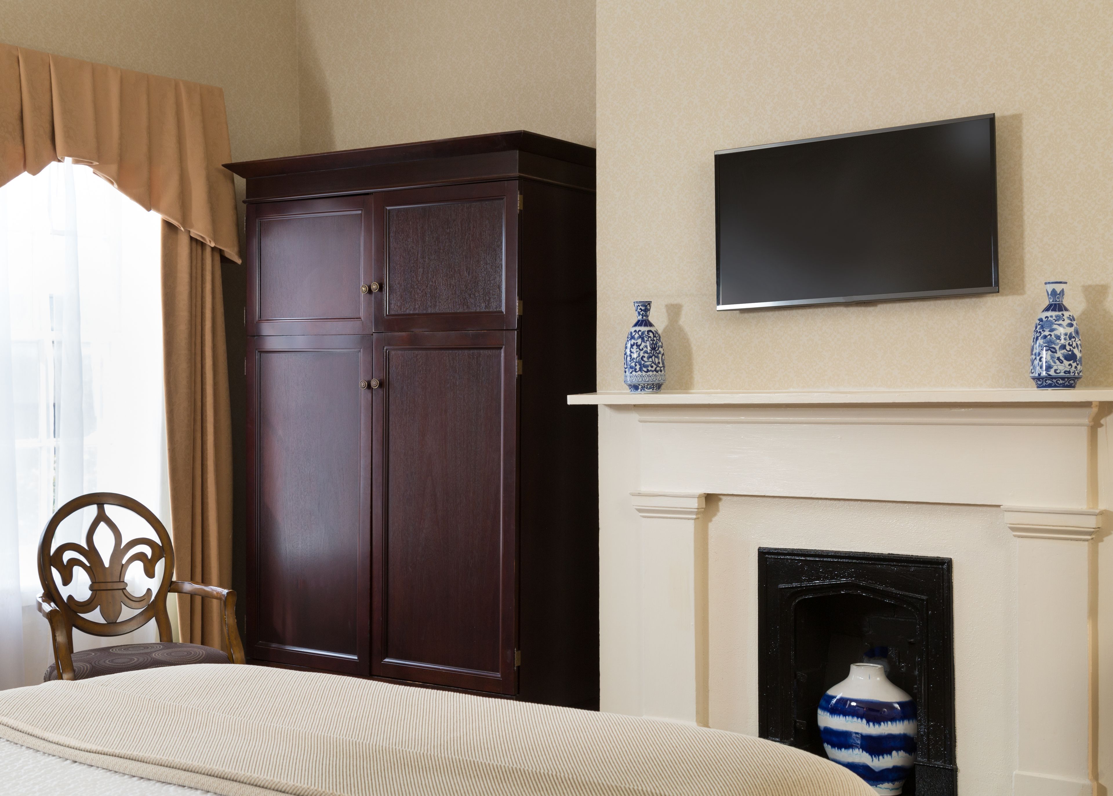 Een slaapkamer met een grote garderobe, een bed, een televisie boven een open haard en decoratieve vazen.