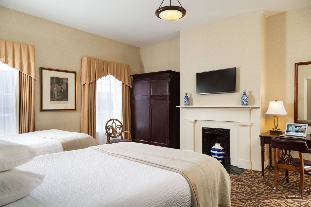 A hotel room with two beds, a television, a fireplace, and a desk with a laptop.