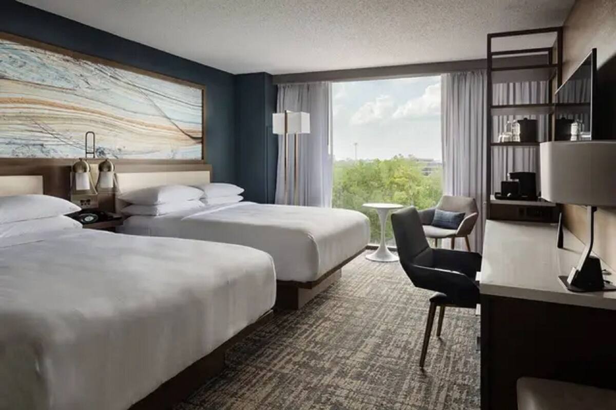 A hotel room with two beds, a desk, a chair, and a large window with a view.