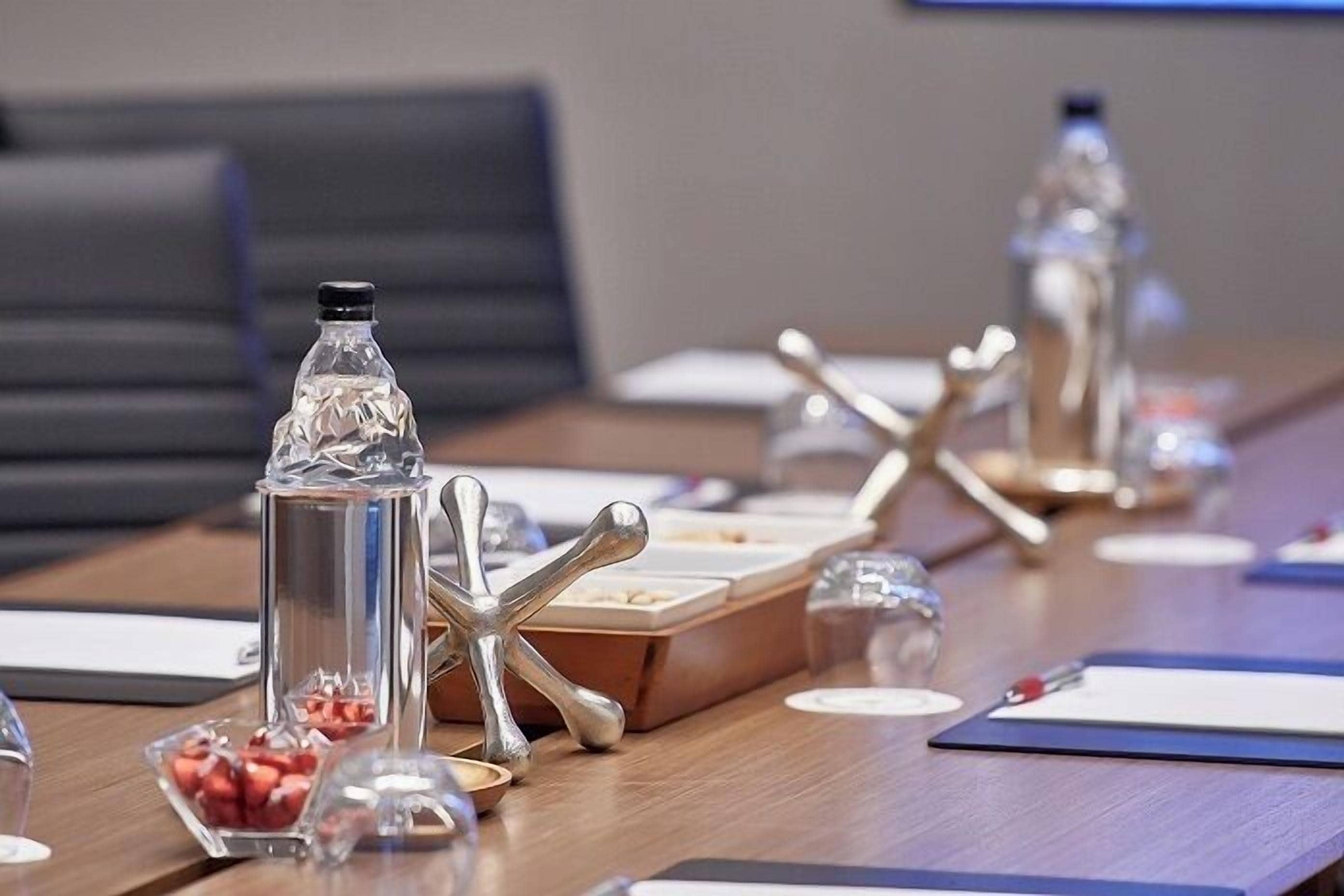 Une table de conférence avec des bouteilles d’eau, une carafe en verre et un saladier de fruits.
