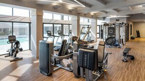 Un gimnasio moderno con máquinas de cardio, equipo de levantamiento de pesas y amplias ventanas con vistas al exterior.