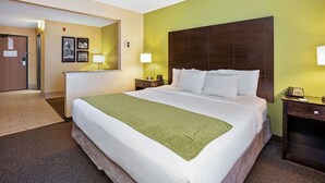 Habitación de hotel con una cama grande, dos mesitas de noche con lámparas, una puerta de madera y una pared decorada con cuadros.