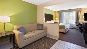 Habitación de hotel con sofá, escritorio, cama, televisor y ventana con cortinas.