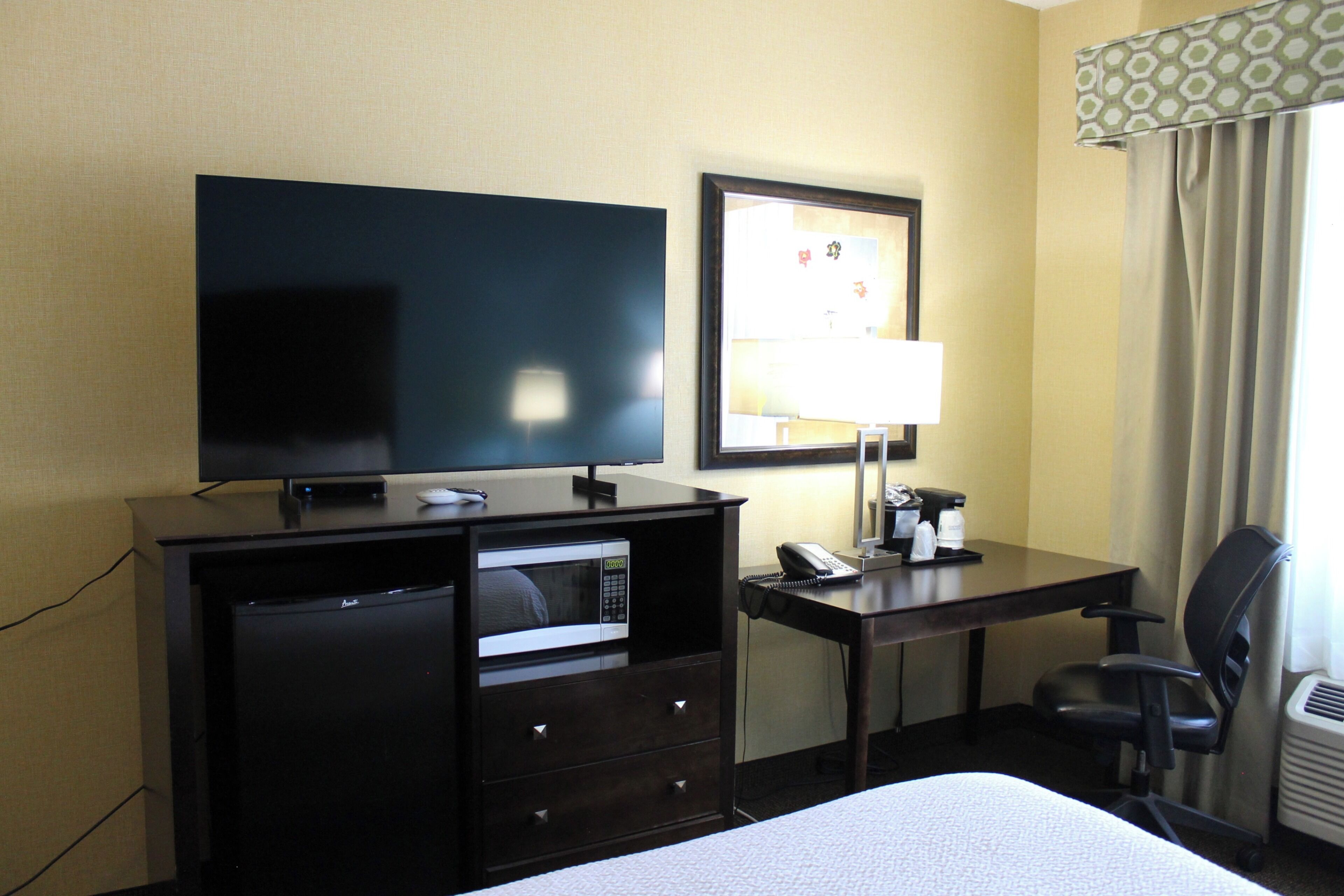Ein Hotelzimmer mit Bett, Schreibtisch mit Computer, Fernseher, Mikrowelle und Telefon.