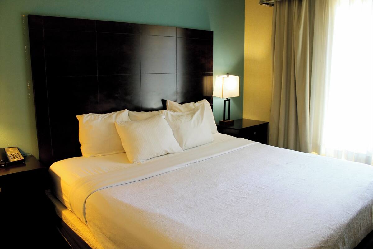 A hotel room with a large bed, a dark headboard, a bedside lamp, and a telephone on the nightstand.