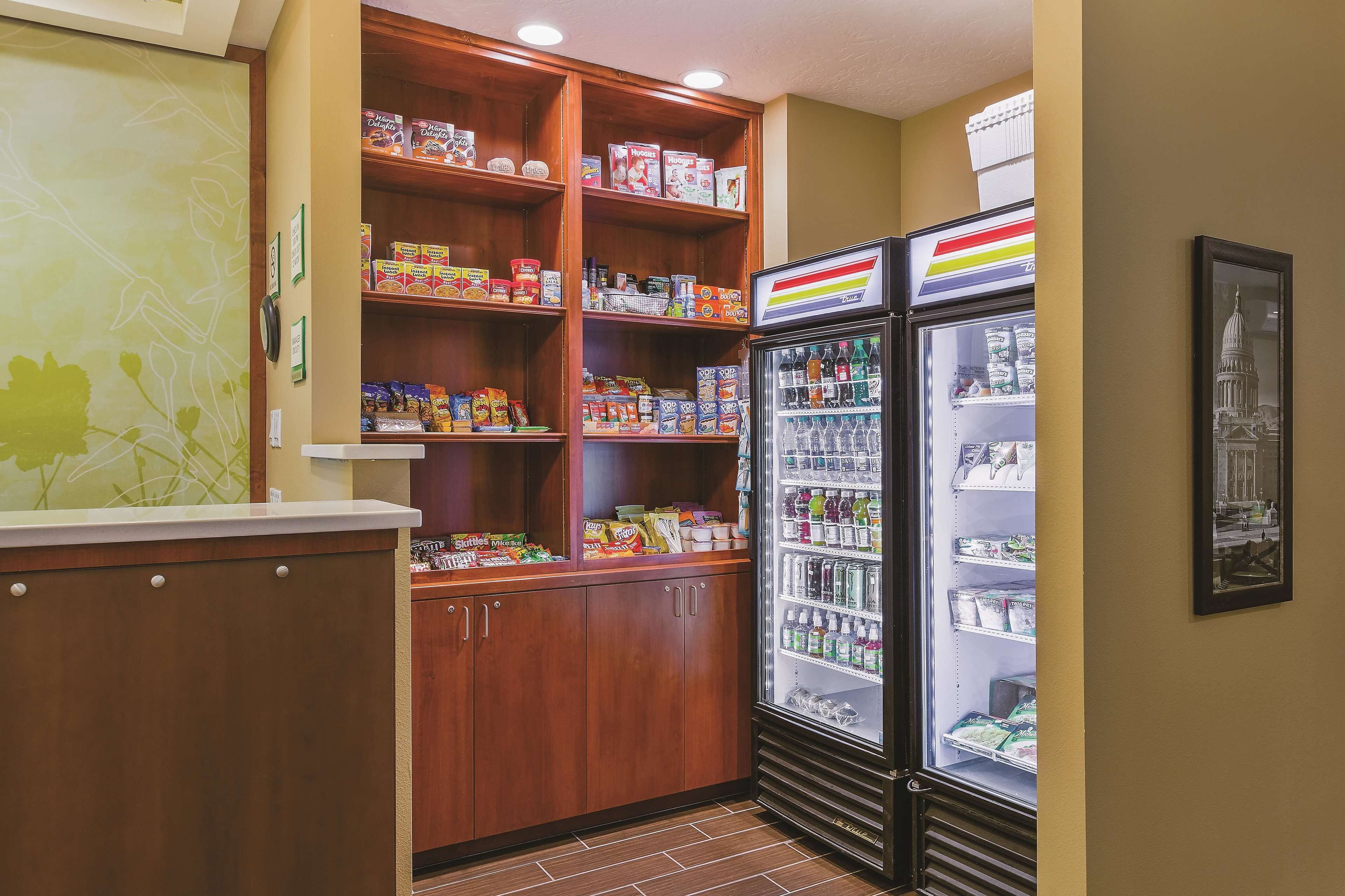 A kitchenette with wooden cabinets, a refrigerator, and a shelf stocked with snacks and beverages.