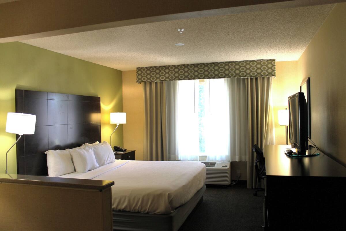 A hotel room with a large bed, two bedside lamps, a flat-screen TV, and a window with curtains.