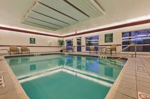 Una piscina con agua cristalina, rodeada de paredes con azulejos, ventanas y algunas sillas.