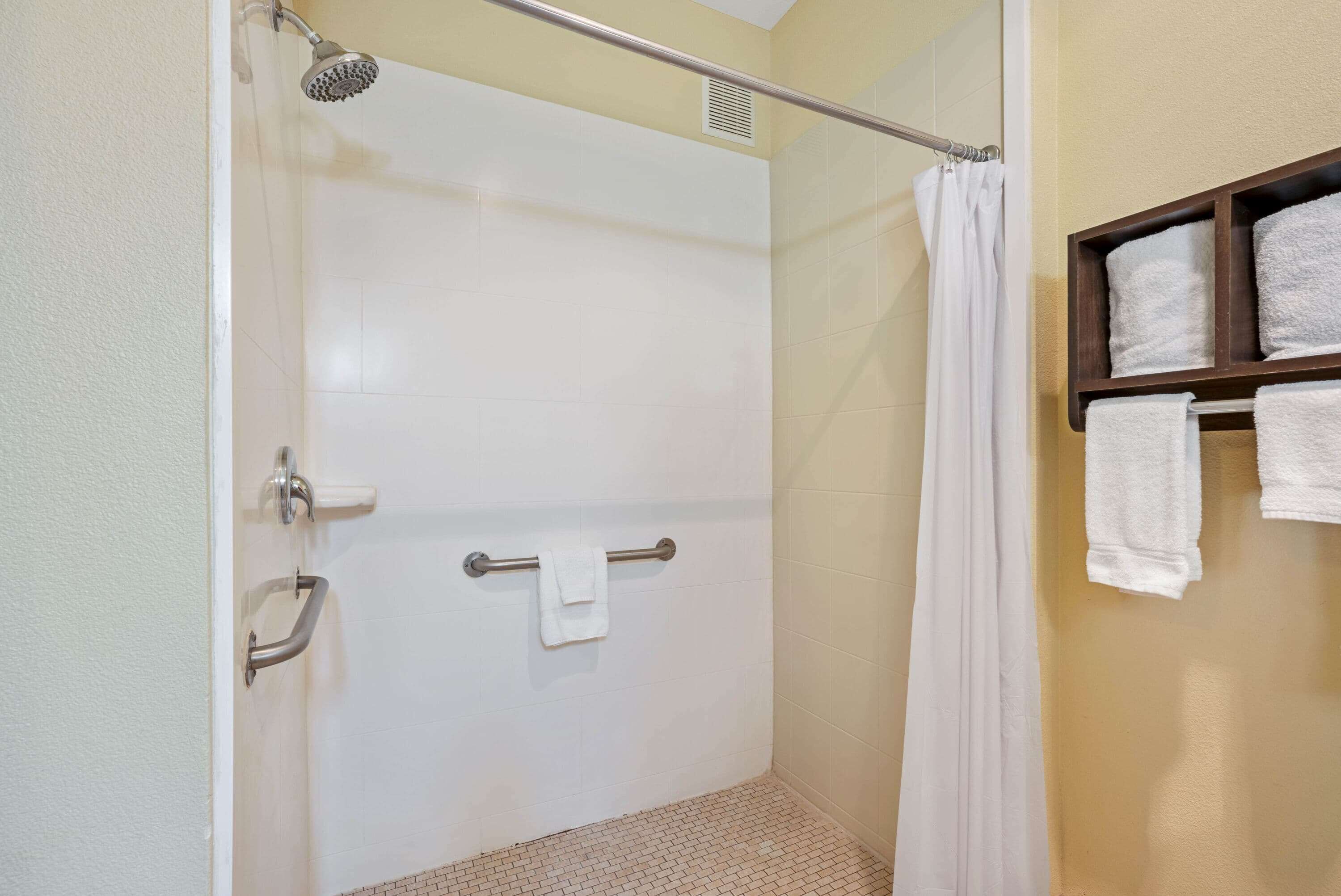 Un espace douche doté d’une porte en verre, d’un porte-serviettes avec une serviette, et d’une étagère en bois avec des serviettes.