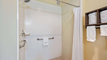Un espace douche doté d’une porte en verre, d’un porte-serviettes avec une serviette, et d’une étagère en bois avec des serviettes.