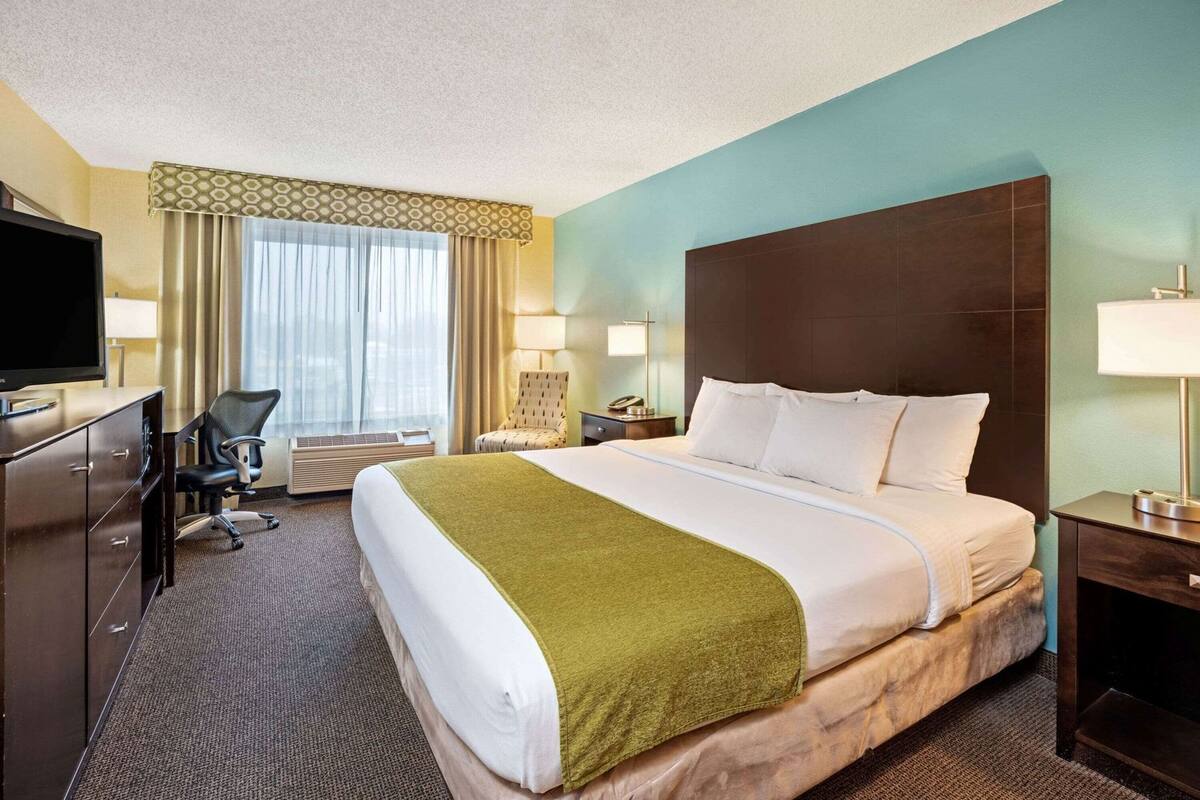 A hotel room with a bed, a desk with a TV, a chair, a desk lamp, and a window with curtains.