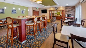 Vestíbulo de hotel con zona de bar, disposición de asientos y un reloj en la pared.