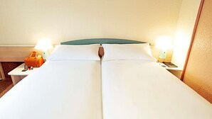 A hotel room with a bed, two bedside tables, a nightstand, a lamp, and a handbag on one of the tables.