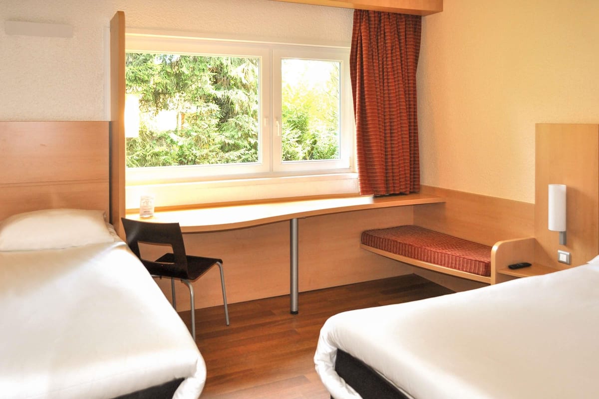 Ein Hotelzimmer mit zwei Betten, einem Schreibtisch, einem Stuhl und einem Fenster mit Vorhängen.