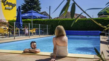 A swimming pool area with a blue pool, a yellow sign, and outdoor seating.