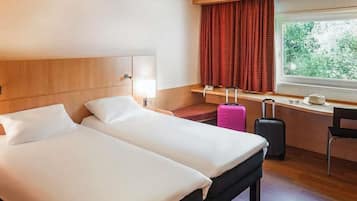 A hotel room with two beds, a desk, a chair, a window with curtains, and a suitcase.