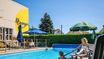Ein Poolbereich mit Liegestühlen, Sonnenschirmen und einem Gebäude mit einem gelben Schild.