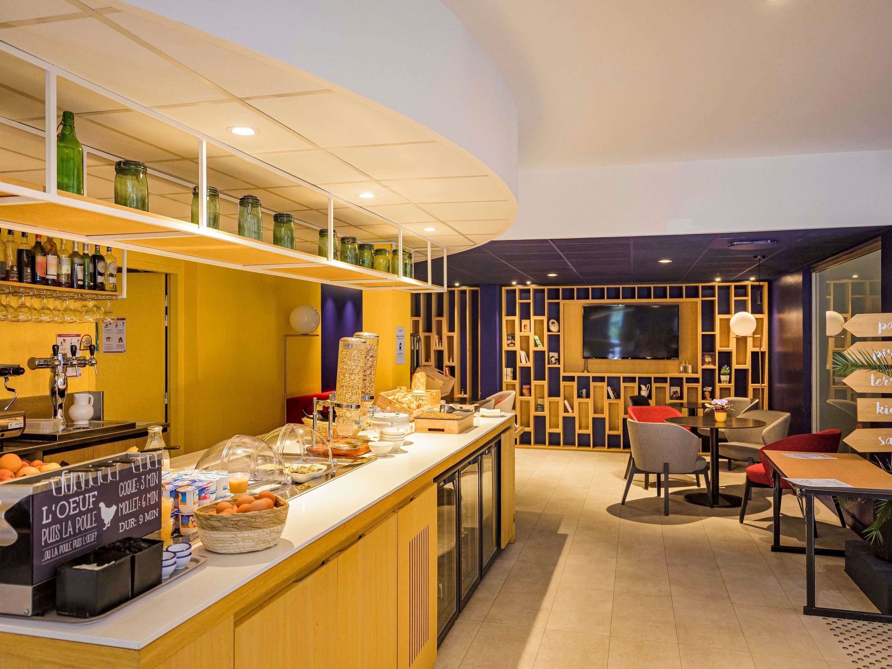 Un comptoir-buffet proposant divers aliments et boissons, un espace détente avec des tables et des chaises, et un téléviseur fixé au mur.