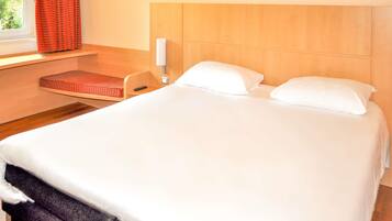 Habitación de hotel con cama, mesita de noche, lámpara y ventana con cortinas.