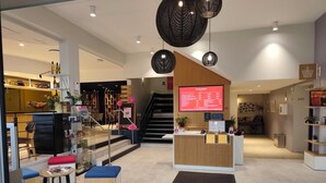 A modern hotel lobby with a reception desk, seating area, and a staircase leading to other floors.