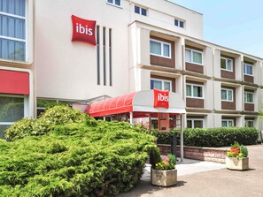 Een hotel met een rood-wit luifel, meerdere ramen en een verzorgde tuin.