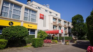 A hotel with a red 'ibis' sign, a yellow 'Camping' sign, and a red canopy over the entrance.