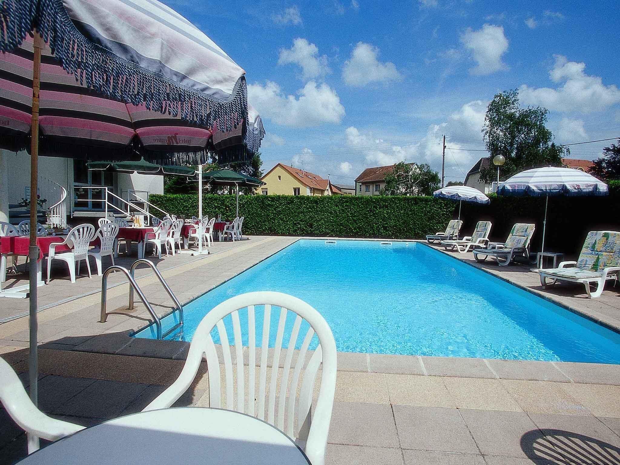 Una piscina amb gandules i ombrelles, envoltada per un bord i edificis al fons.