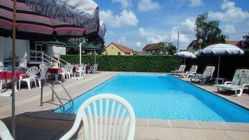 Una piscina amb gandules i ombrelles, envoltada per un bord i edificis al fons.