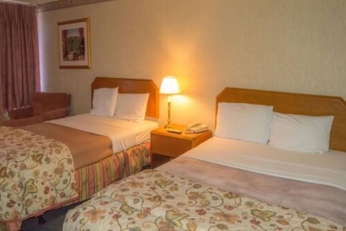 A hotel room with two beds, a nightstand with a lamp, a chair, and a framed picture on the wall.