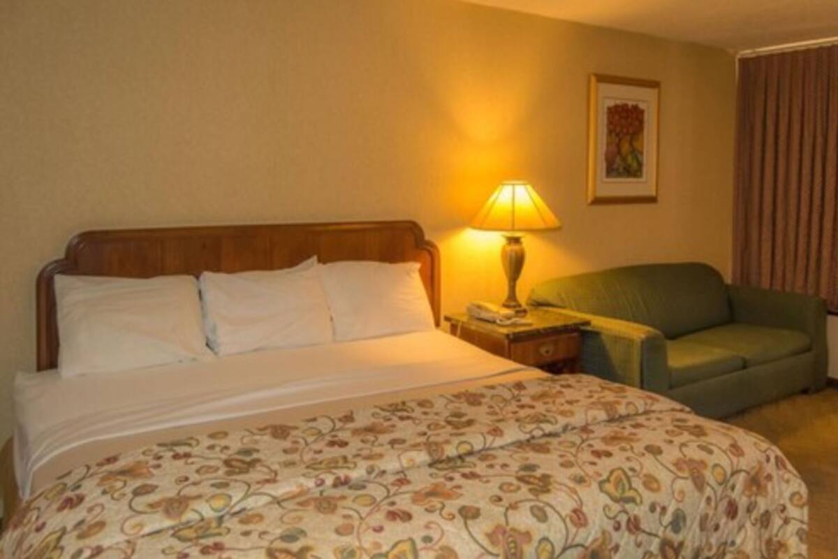 A hotel room with a bed, a nightstand with a lamp, a green armchair, and a framed picture on the wall.