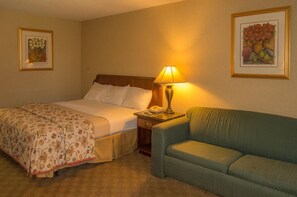 Una camera d'albergo con un letto, un comodino con una lampada, un divano verde e due quadri appesi alle pareti.