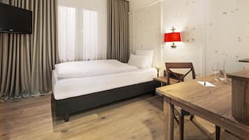 Una habitación de hotel con cama, una mesa de madera, una silla, un televisor y una lámpara de pared.