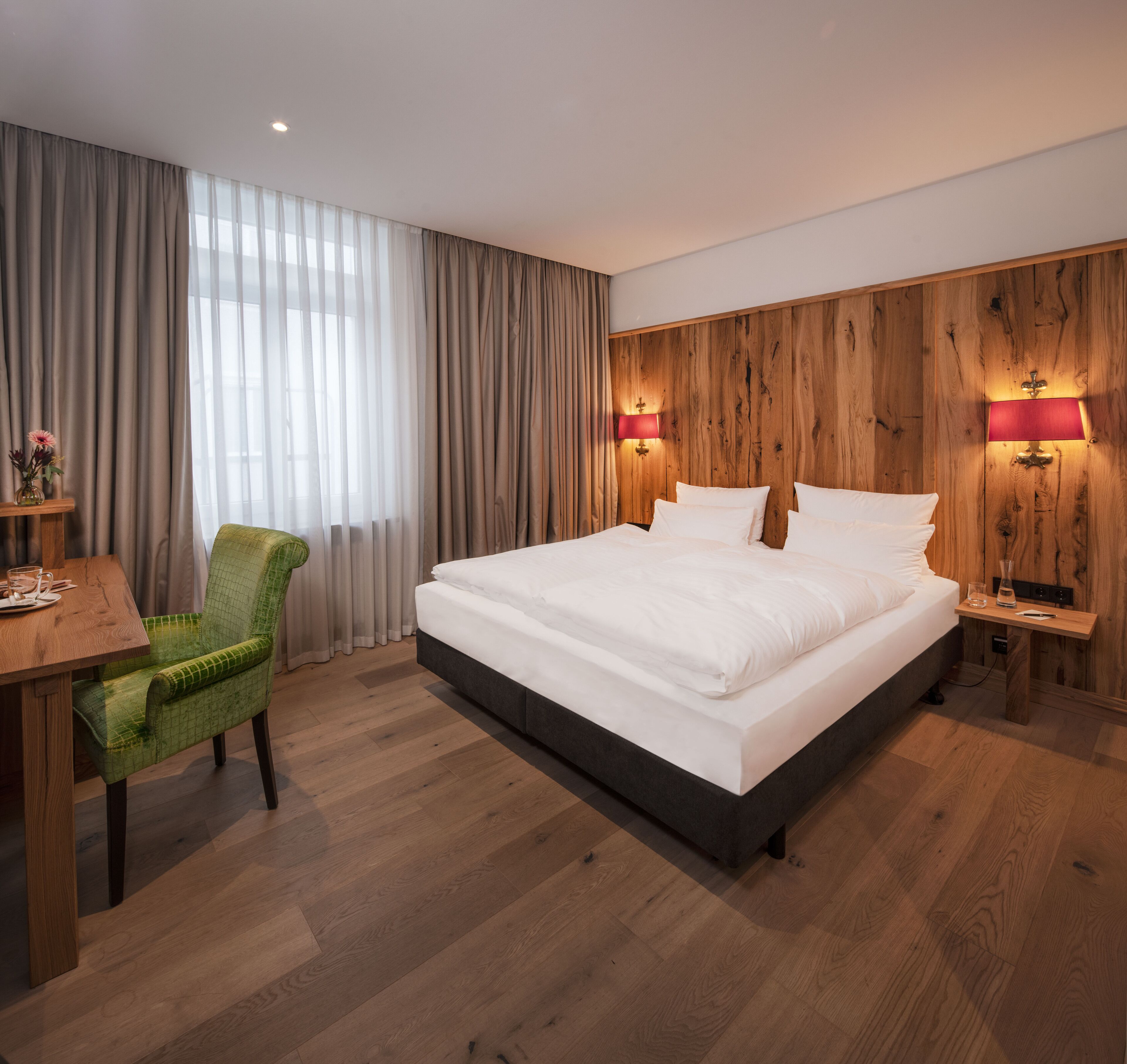 Een hotelkamer met een groot bed, houten paneelwanden, een bureau met stoel en twee bedlampjes.