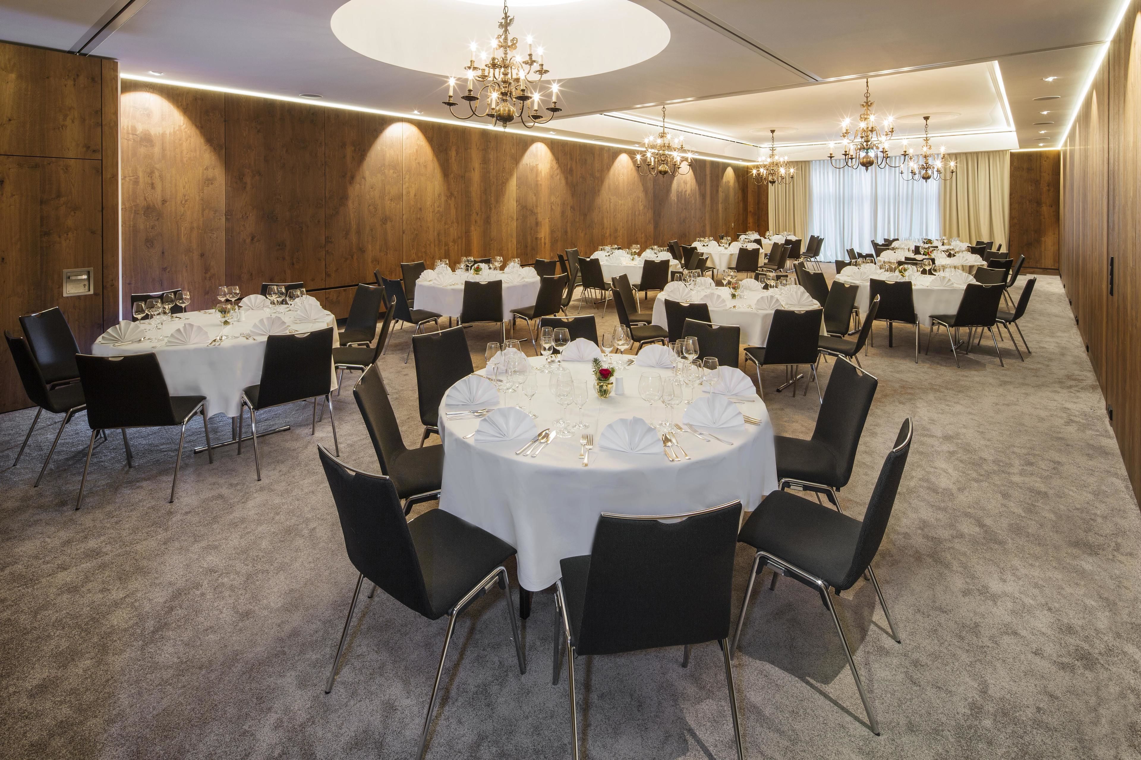 A conference room with round tables, black chairs, and chandeliers.